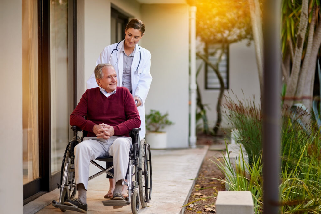 He loves a trip around the garden. an elderly man in a wheelchair being assisted by a nurse outside a clinic.